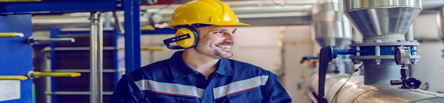 Dedicated smiling factory worker standing next to boiler and hol