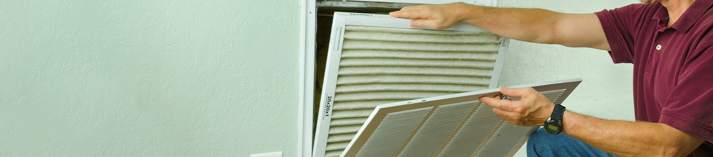 Man replaces air filter behind panel.